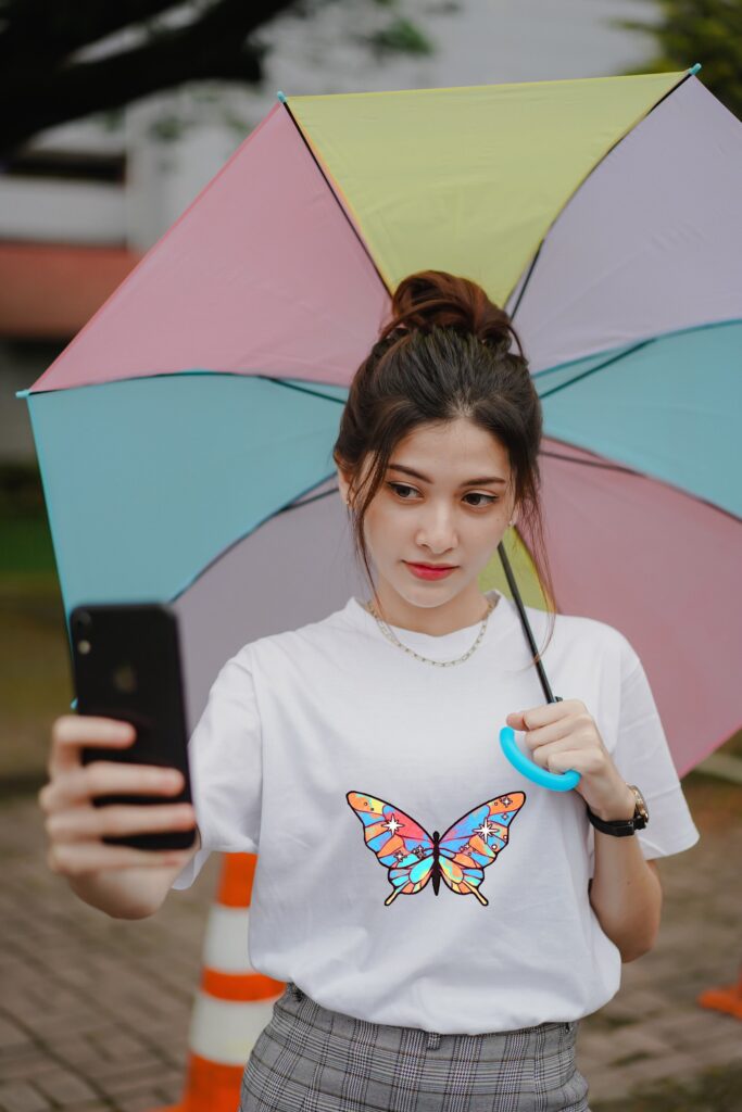 woman holding a colorful umbrella wearing a white tshirt with a butterfly on the front