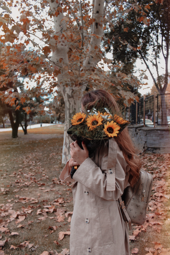 woman holding sunflowers to hide her face in fall