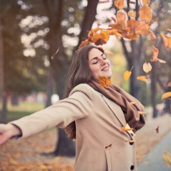 woman throwing up fall leaves in park