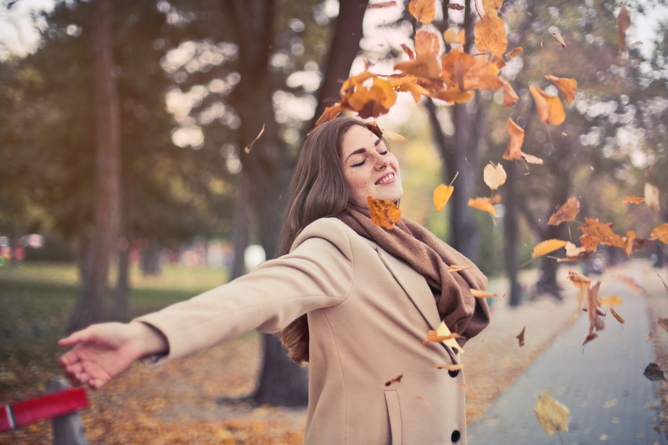 woman throwing up fall leaves in park