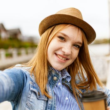 woman with red hair wearing a hat and taking a selfie