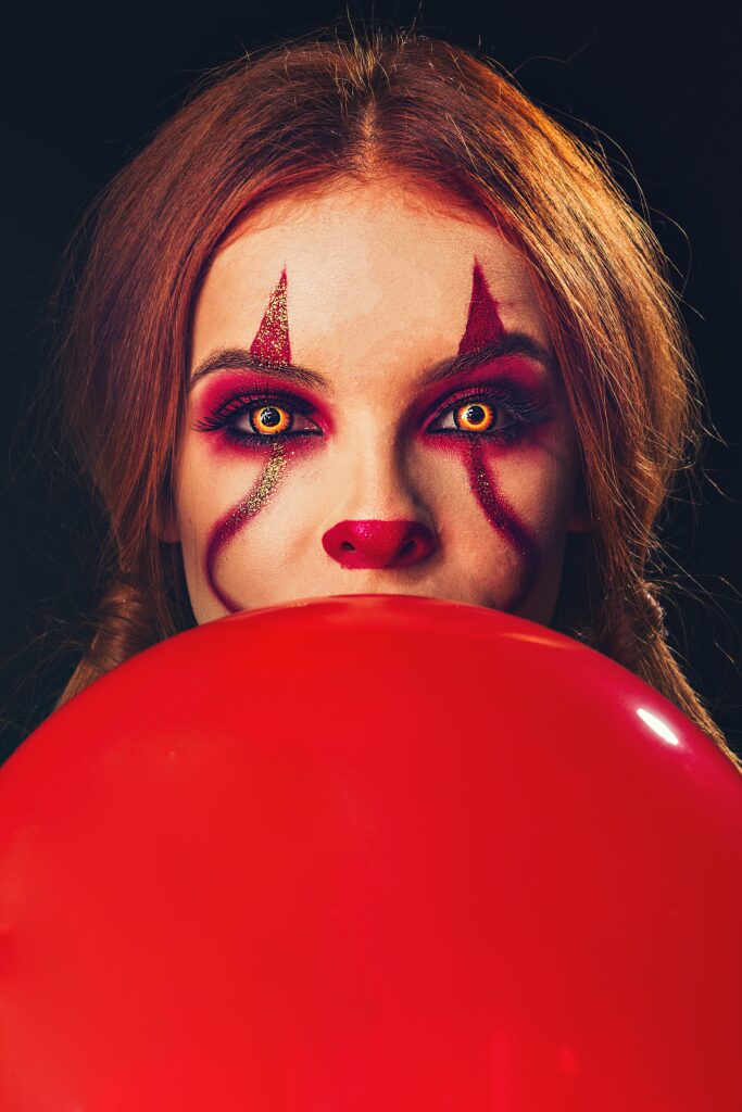 Woman wearing scary clown makeup holding a red balloon