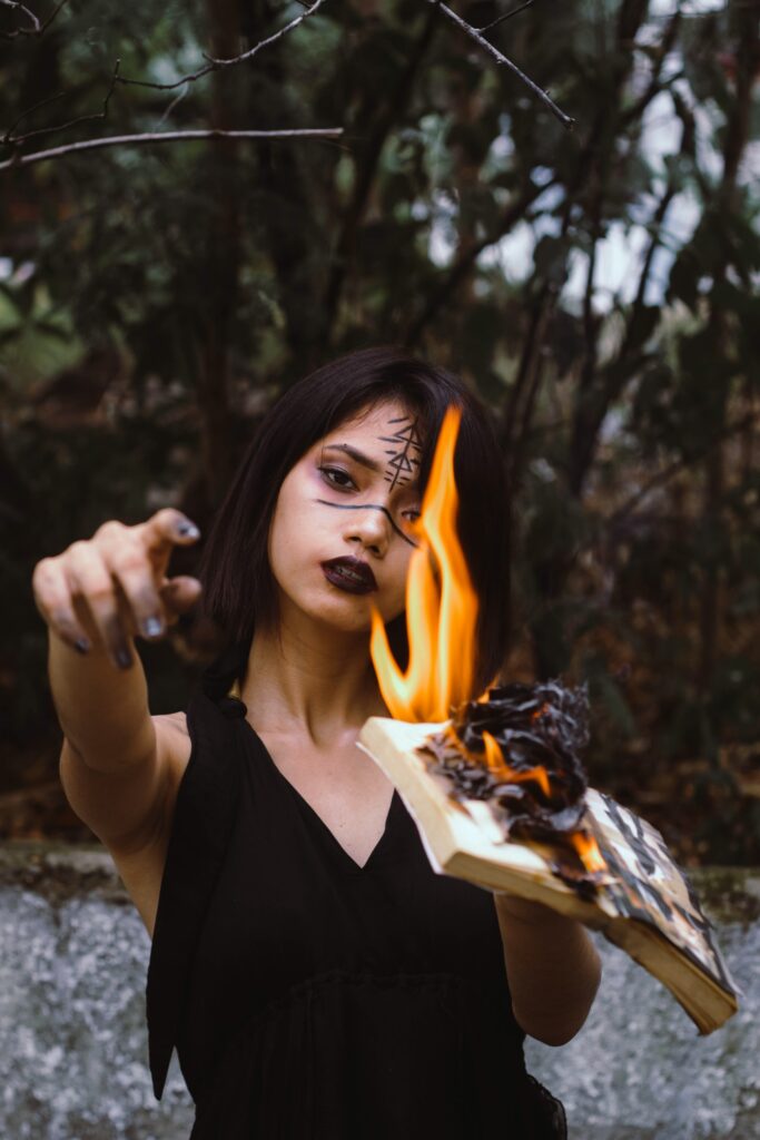 Woman dressed as a witch holding a book on fire in the woods