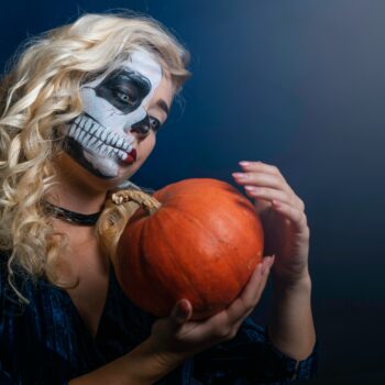 Woman wearing skull makeup and holding a pumpkin