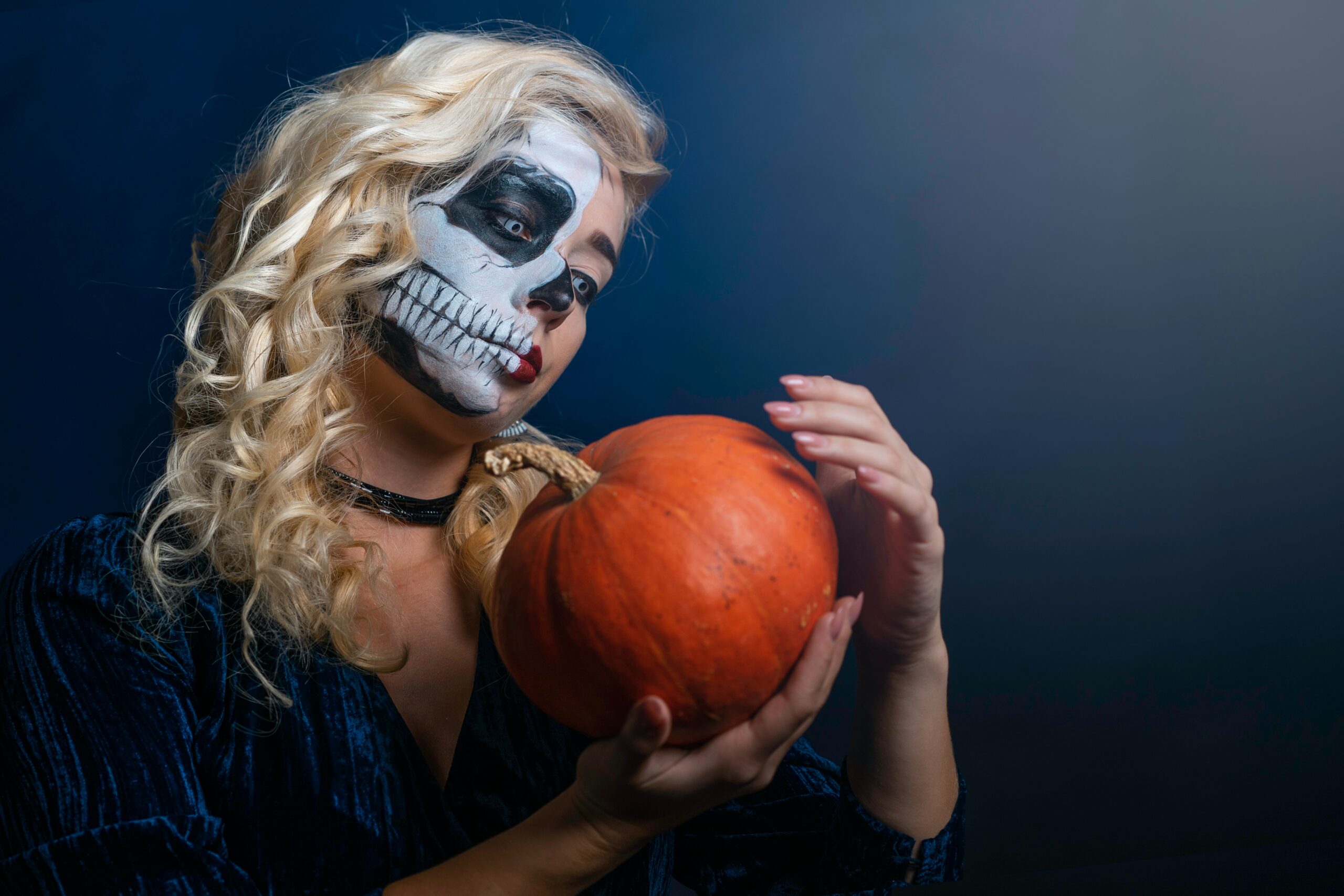 Woman wearing skull makeup and holding a pumpkin