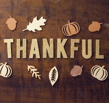The word "Thankful" spelt out on a wooden background surrounded by fall iconss