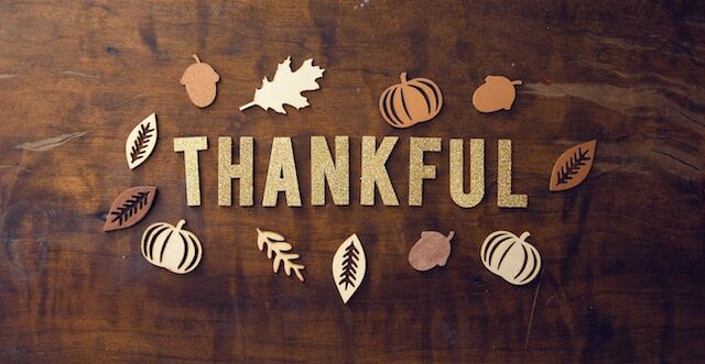 The word "Thankful" spelt out on a wooden background surrounded by fall iconss